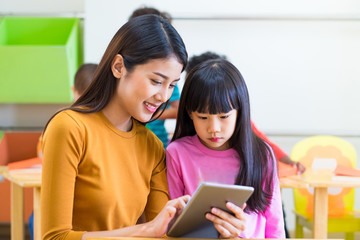 Asia woman teacher teach girl student with tablet computer in classroom at kindergarten...