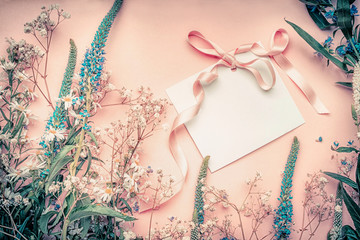 Blank white paper card with flowers on pastel background, top view.Lovely greeting card or invitation for wedding, Mothers day or happy event