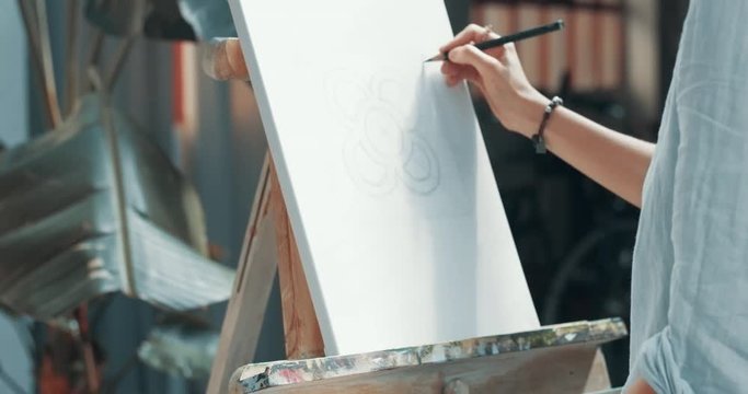 Attractive young girl draws a sketch with pencil on canvas in her studio