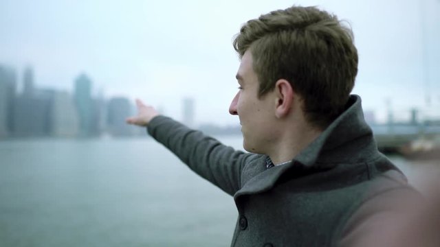 Young man holding the camera in front of his face and talking while shooting himself with Manhattan island on a background