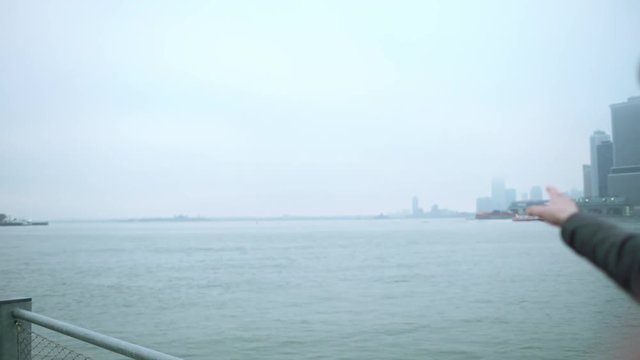 Happy young man talking while shooting himself with camera in front of his face and pointing to Manhattan island in the distance