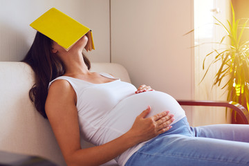 Pregnant woman tired of reading, sleeping on sofa with a book on her face