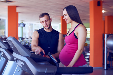 Pregnant woman exercising on treadmill with personal trainer