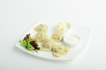Dumplings with butter, sour cream and greens on a plate isolated on white background