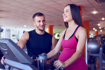 Fototapeta na wymiar Happy pregnant woman running on treadmill under control of personal trainer