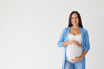 Loving woman touching pregnant belly against white background