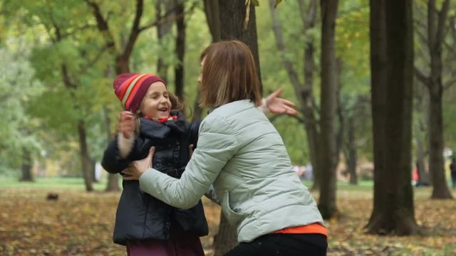 Cute little girl come running to her mother, mom lifts her into her arms and whirls with her in the autumn park. Slow motion.