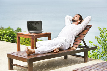 Businessman wearing white using laptop on the beach