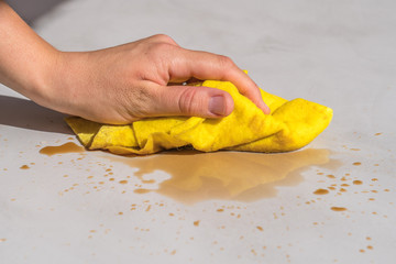 woman's hand cleaning tea stain or spilled coffee on a cement floor with a yellow floor cloth dishcloth closeup