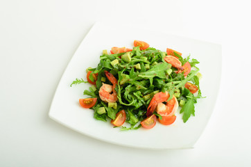 Salad with shrimps, avocado, cherry tomatoes and arugula on a plate isolated on white background