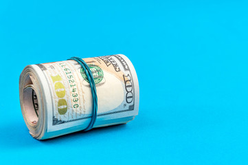 US one hundred dollar bills rolled up with rubber band on a blue.