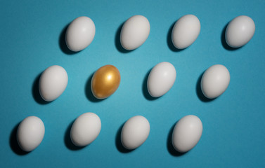 Concept of individuality, exclusivity, better choice. One golden egg among white eggs which are disposed in the diagonal rows on blue background.