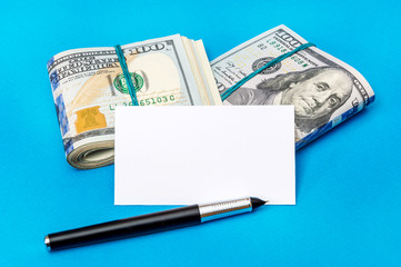 Two packs of folded dollar bills with blank business card and pen on a blue background.