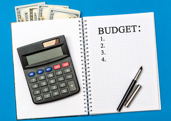 Budget list on a notepad with money and calculator on a blue. Budget planning concept. Top view.