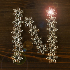 The letter "N" is made up of Christmas stars. Christmas alphabet on a dark wooden background. Selective focus.