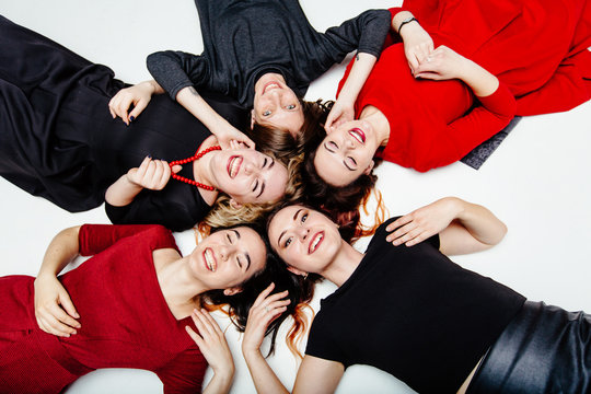 Top View Of Five Girls Lying In A Circle. Woman In Black And Red Dresses Lying On The White Floor And Laughing Merrily. Girls Lying On The Back. Female Group Of Five, People, Fun, Hen-party Concept.