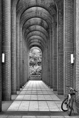 Bike Leaning on the front part of an arcade. A black and white image of a bike leaning on arcade. There are two white street lamps fixed on arch. 
