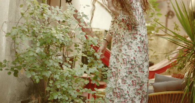 Young woman in floral dress with long hair taking care of a backyard garden