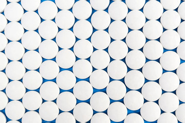 Medical background of white round pills on blue. Top view.