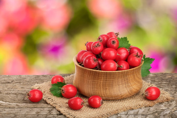 Hawthorn berry with leaf in a bowl on wooden table with a blurry garden background