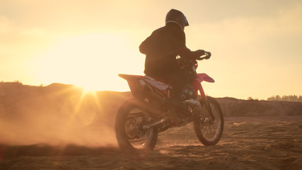 Fototapeta na wymiar Professional FMX Motorcycle Rider Twists Full Throttle Handle and Starts Riding on the Sandy Off-Road Track. Scenic Sunset.