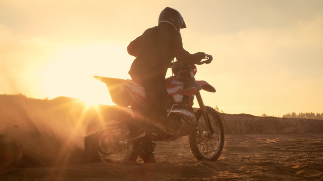 Professional FMX Motorcycle Rider Twists Full Throttle Handle and Starts Riding on the Sandy Off-Road Track. Scenic Sunset.