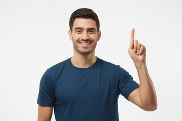 Attractive young man in blue t-shirt pointing up with his finger isolated on gray background