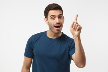 I got a solution! Photo of energetic nice smiling man wearing blue t-shirt isolated on gray background pointing finger in eureka sign, having great innovative idea, understanding