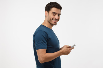 Young attractive male looking and smiling at the camera with cheerful expression while texting his...