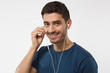 Happy young man with beautiful smile, holding earphone with hand, talking with friend about his favourite music