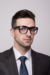 Portrait of a young and fashion businessman with nerd glasses on gray