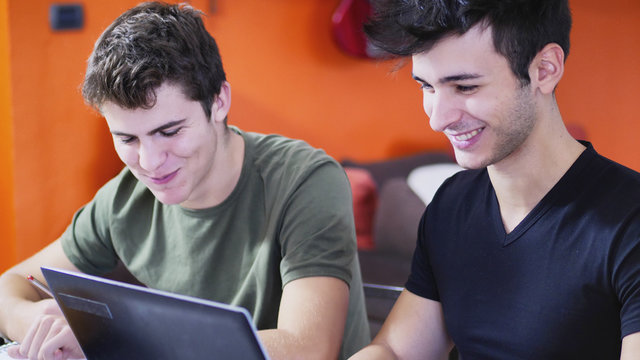 Two young friends doing homework with laptop computr and tablet PC while sitting at table with notebooks.