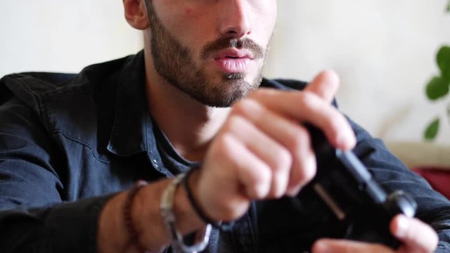Attractive young man using joystick or joypad for videogames, sitting on couch at home in his living room, staring at TV screen