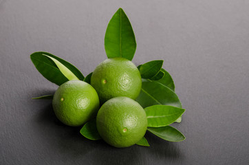 three green limes with leaves on a gray background
