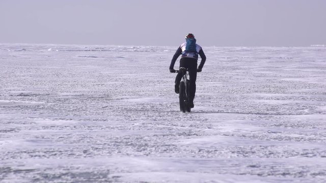 a sportive man riding a bicycle across a frozen lake
