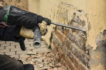 Worker with electrical hammer cleaning red brick wall outdoor