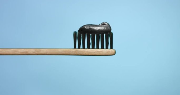 Black toothpaste on toothbrush with black bristles and wooden handle isolated on colorful backgrounds