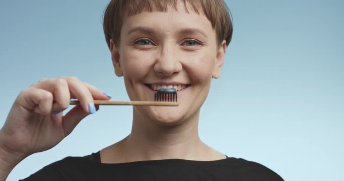 Happy smiling attractive young woman brushing her teeth with black toothpaste and having fun