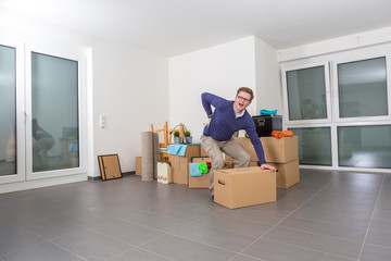 Mann hat Rückenschmerzen beim Heben eines Kartons während des Einzugs in eine neue Wohnung