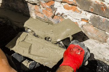 Worker with wall plastering tools renovating house. Plasterer renovating outdoor foundation and...