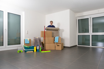 Mann reinigt eine große, helle, leere Luxuswohnung, dabei rollt er einen Teppich zusammen.