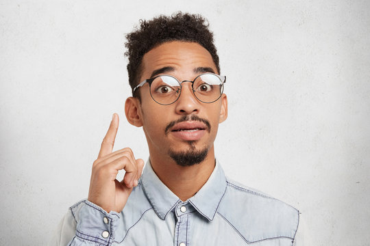 I get great idea. Confident mixed race male scientist wears roung glasses, has mustache and beard, raises finger up, develops new strategy of work, has inspiration and new interesting thoughts