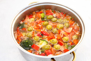 Vegetable soup of tomatoes, peppers, broccoli and olives cooked in a saucepan.