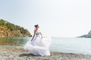 Fototapeta na wymiar Beautiful young bride standing on the beach near the sea