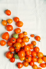 Fresh organic tomatoes of different colors on white textile background. Harvest concept. Overhead view, natural lighting, copy space.
