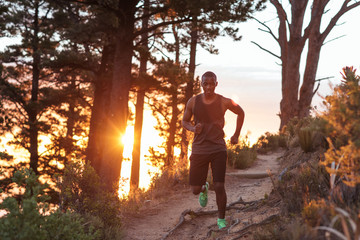 Young African man cross country running along trail at dusk