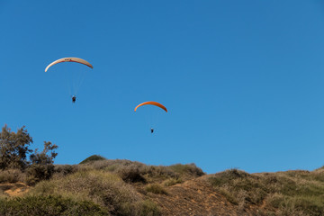 Two paragliders in the air, above a meadow