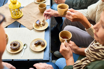 High angle of several senior people drinking tea with chocolate doughnuts meeting in outdoor cafe round table - Powered by Adobe