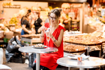Young woman in red dress eating jamon traditional spanish dry-cured ham sitting at the Barcelona food market