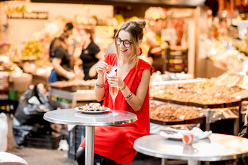 Young woman in red dress eating jamon traditional spanish dry-cured ham sitting at the Barcelona...